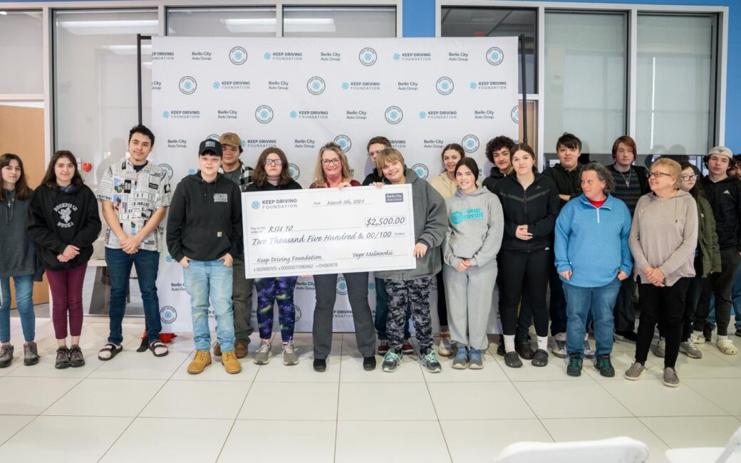 A group photo of adults and children holding a giant money check for $2,500 from the Keep Driving Foundation
